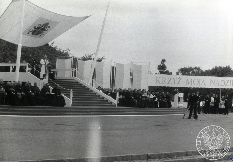 Jan Paweł II wygłasza homilię podczas spotkania z młodzieżą na Westerplatte, u podnóża podestu siedzą hierarchowie kościelni, widoczny transparent: „Krzyż Moja Nadzieja” 12 VI 1987 r., IPN Gd 003/200 t. 7.