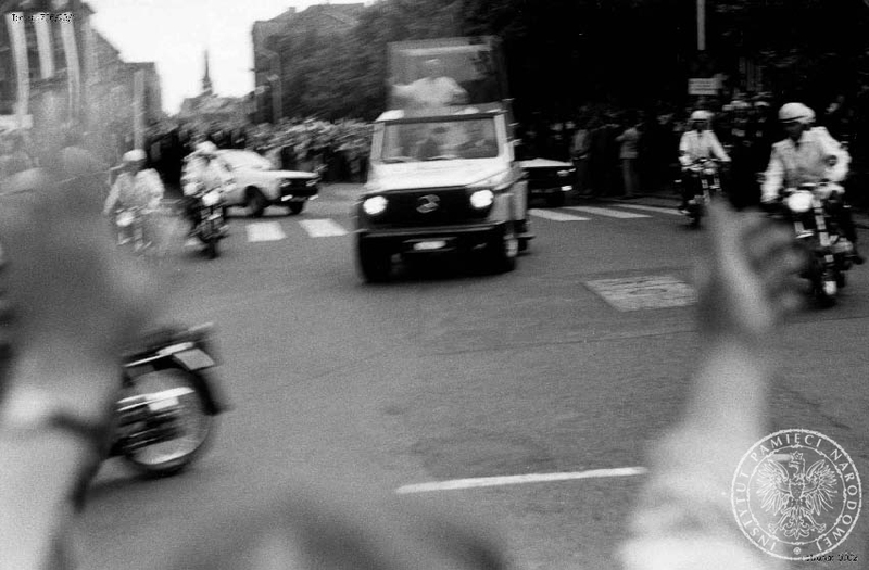 Jan Paweł II w papamobile, w asyście milicjantów na motocyklach, przejeżdża ulicami Szczecina pozdrawiany przez wiernych. 11 VI 1987 r. IPN Sz 706/23 t. 1-2.