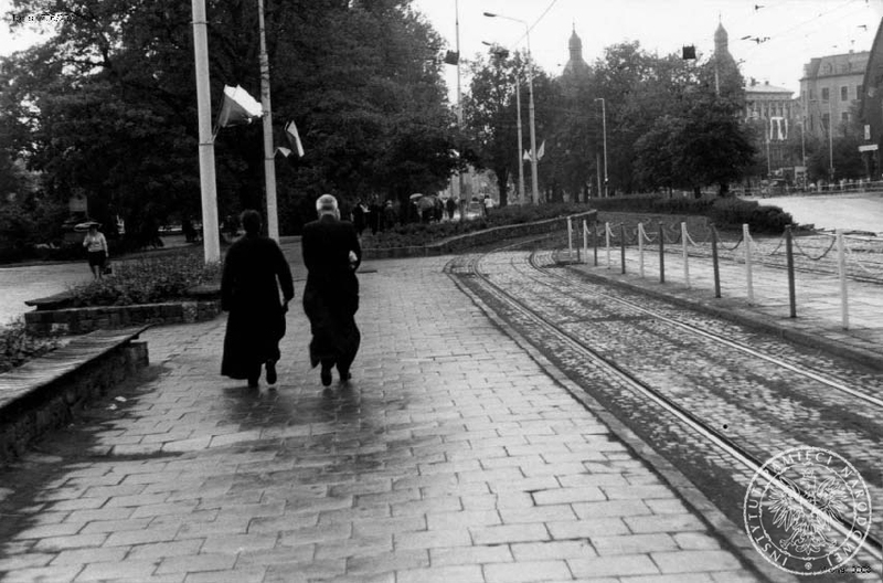 Dwóch księży na udekorowanej flagami Polski ulicy Szczecina w trakcie pobytu w tym mieście Jana Pawła II. 11 VI 1987 r. IPN Sz 706/23 t. 1-2