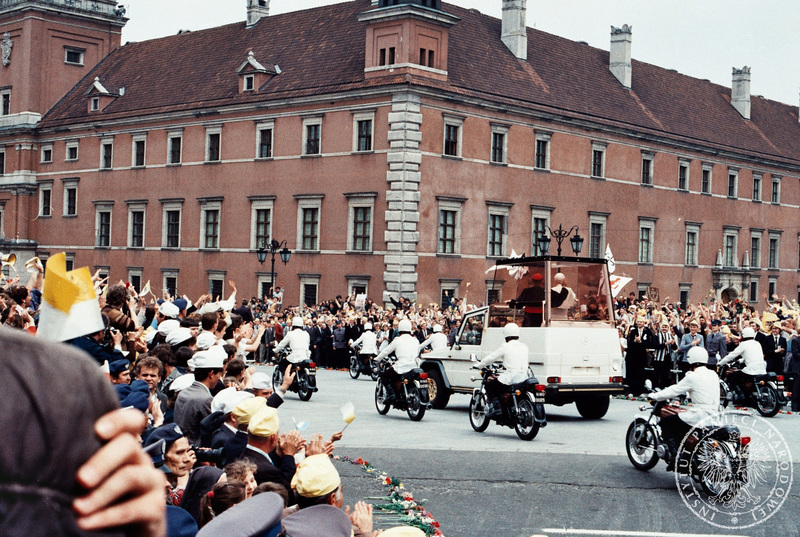Jan Paweł II i prymas Polski Józef Glemp w papamobile w asyście milicjantów na motocyklach wjeżdżają na Plac Zamkowy pozdrawiani przez wiernych. W tle Zamek Królewski. 14 VI 1987 r. IPNBU-7-7-8-314